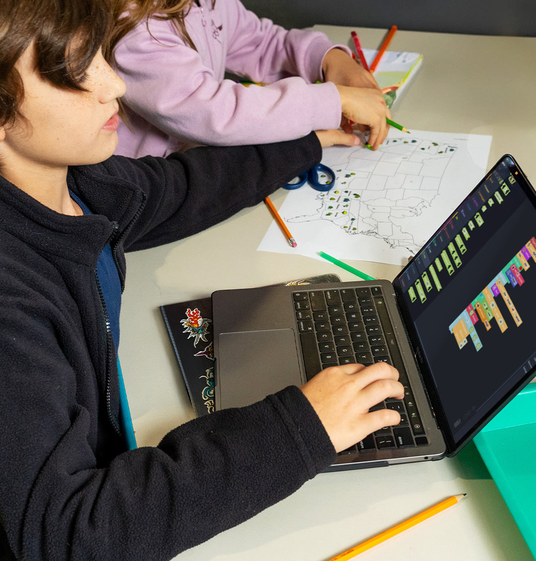 Students using the Ozobot Editor on a laptop while working on coding activiy with pencils and paper